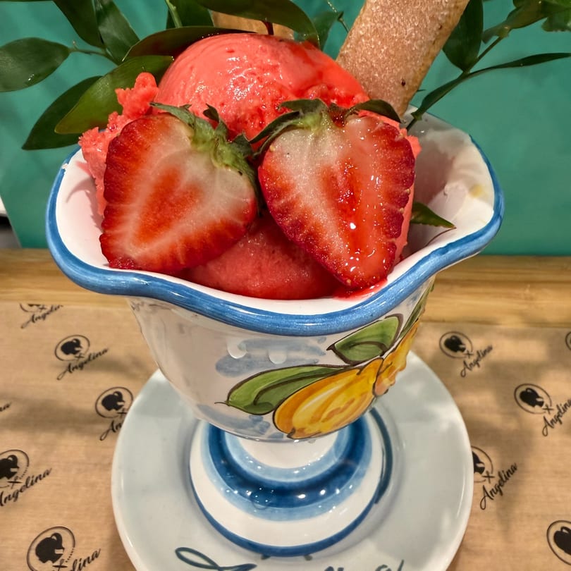 Strawberry sorbet with fresh strawberry halves and a cookie stick in a decorative bowl.
